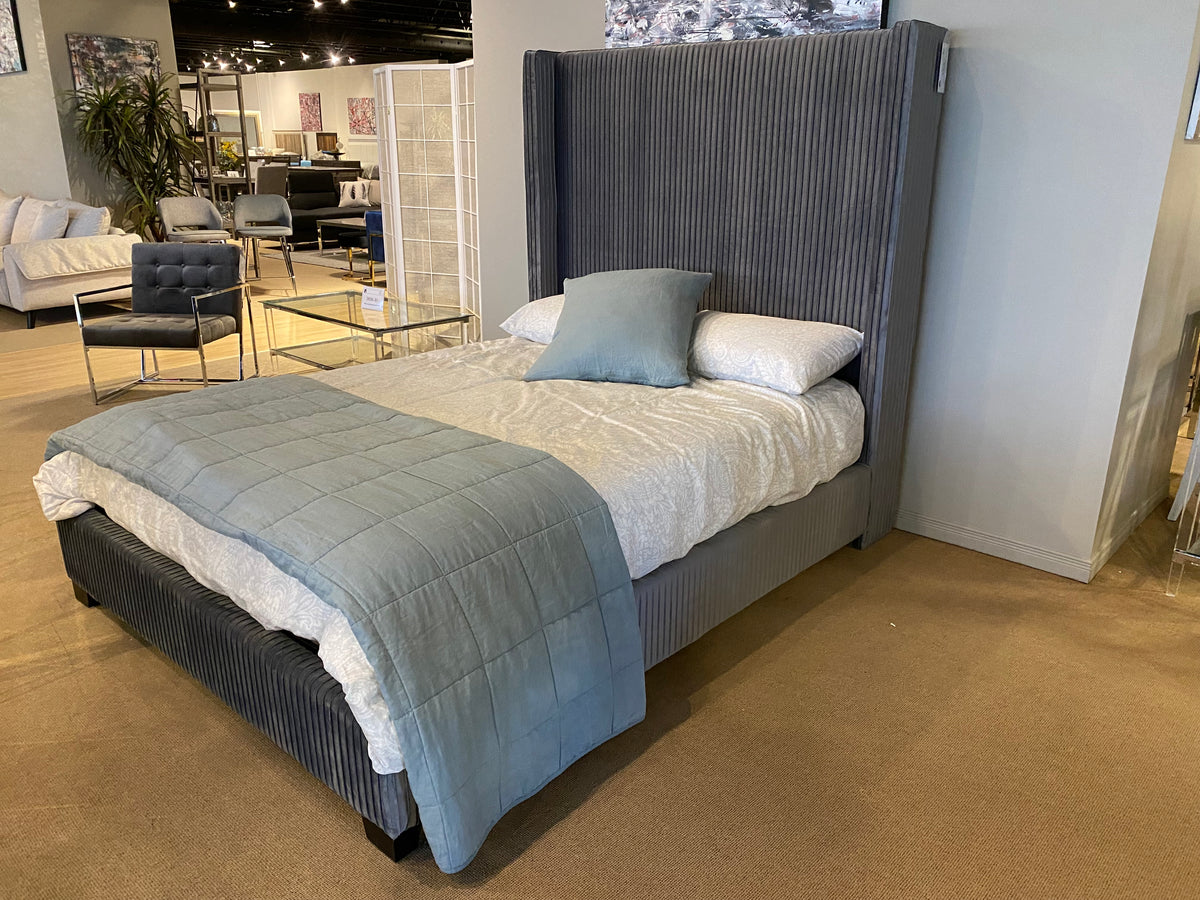 Model 1547 grey upholstered bed with tall vertical channel-tufted wingback headboard in a showroom